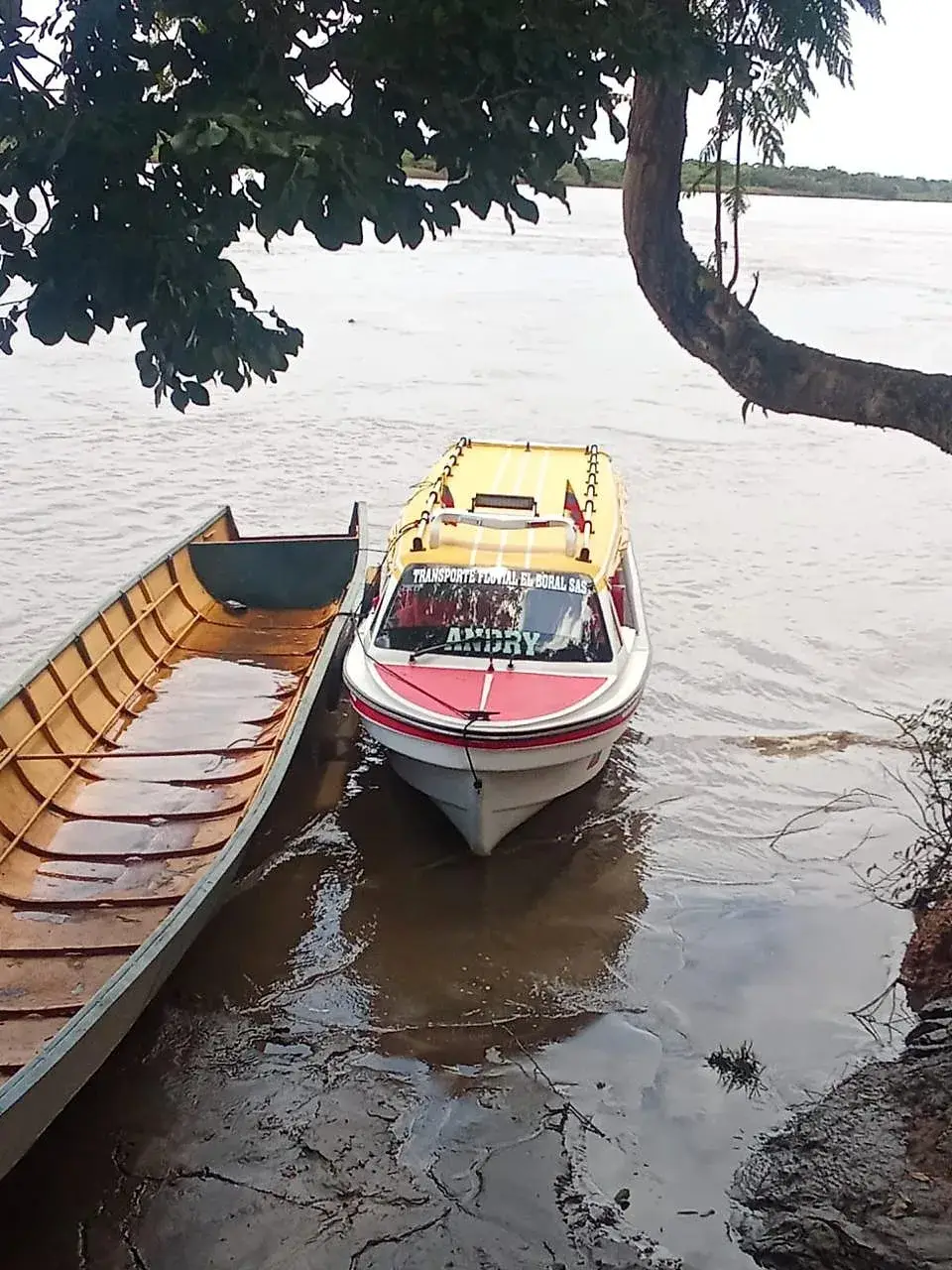 Yate de pasajeros junto a una canoa en la orilla del río.